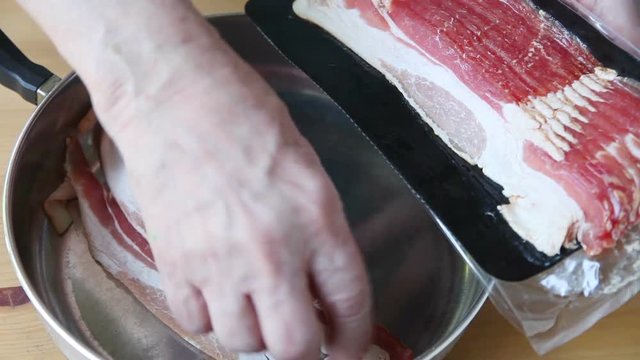 A man places raw bacon into a skillet