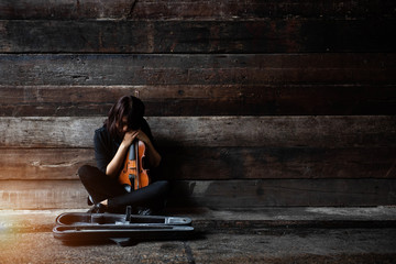 The lady is sitting on grunge surface cement floor,hold violin and bow in her arms,turn face down...