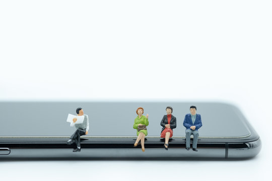 Technology And Communication Concept. Group Of Man And Woman Miniature People Figures Sitting And Talking On Smart Phone On White Background.