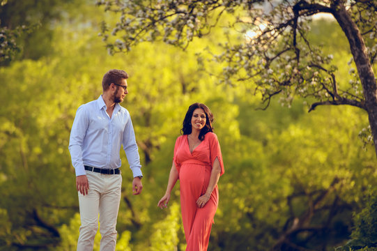 Romantic portrait of young smiling happy couple of lovely future parents during sunset on nature apple tree background in the city park. Pregnancy pregnant future mother photoshoot. Motherhood photo
