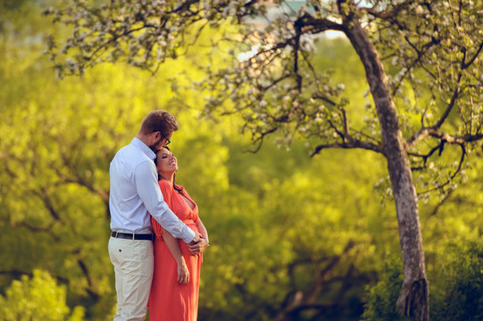 Romantic portrait of young smiling happy couple of lovely future parents during sunset on nature apple tree background in the city park. Pregnancy pregnant future mother photoshoot. Motherhood photo