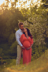 Romantic portrait of young smiling happy couple of lovely future parents during sunset on nature apple tree background in the city park. Pregnancy pregnant future mother photoshoot. Motherhood photo