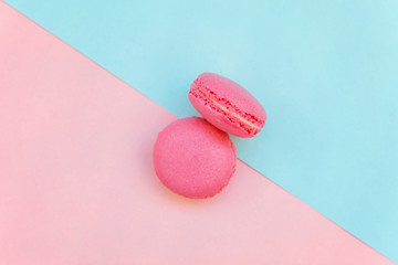 Top view of mini pink macaron or macaroon french desserts cake on soft sweet pink and blue pastel geometric paper flat lay background
