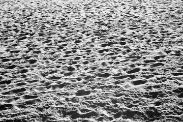 Ein Sandstrand in schwarzweiss mit unzähligen Fussabdrücken und Fussspuren schaut aus wie eine Kraterlandschaft auf dem Mond © Thomas