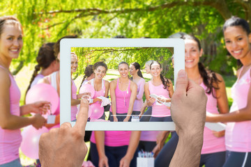 Hand holding tablet pc against smiling women organising event for breast cancer awareness