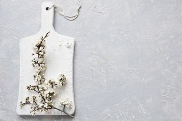 Close-up photo of beautiful white blooming flowers of cherry tree branch on white wooden cutting board on grey background