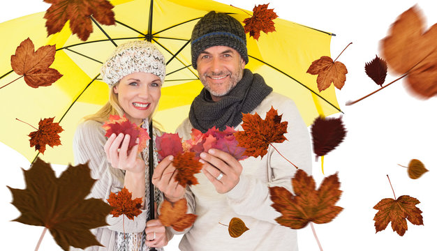 Portrait of couple holding autumn leaves while standing under yellow umbrella against autumn leaves pattern