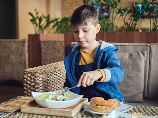 Cute Caucasian boy enjoying a Caesar salad at a cafe.