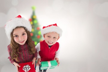 Cute siblings with gifts against blurry christmas tree in room
