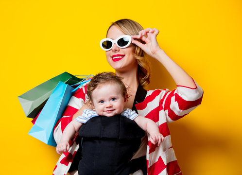 Mother and little baby in carrier have a shopping with bags. Models on yellow background