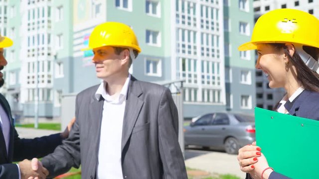 businesspeople holding engineers in the hands of drawings rolled up. business people in costumes at a construction site. two men and women. mixed races group. 4л