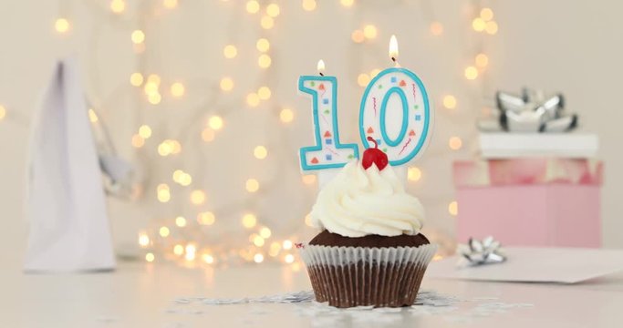 Birthday cake with burning candle as number ten on blurred garland lights background