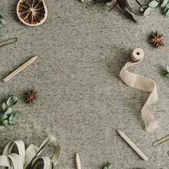 Frame of eucalyptus branches, pencils, dry oranges on beige blanket background. Flat lay, top view rustic mock up.