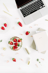 Female stylish home office desk with laptop, notebook, lipstick, fresh raw strawberries and rose flower buds on white background. Flat lay, top view.