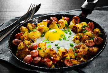 fried egg with sausage and potato in a frying pan on wooden table