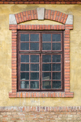 Old window on yellow building facade, with decorative brick frame and arch