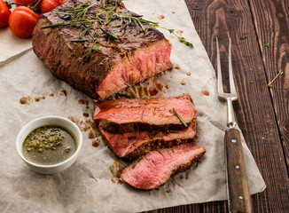 Sliced Roast beef on white paper on wooden table with grilled vegetables.