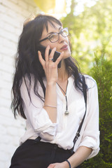 Beautiful business woman talking on the phone. A successful female with glasses is holding a smartphone in her hand on a summer street. 