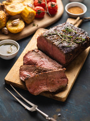 Sliced Roast beef on cutting board with grilled vegetables .