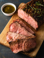 Sliced Roast beef on cutting board with grilled vegetables .