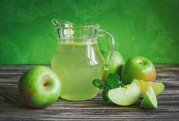 A decanter of apple juice with green apples on a wooden table, close-up