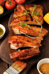 Delicious barbecued ribs seasoned with a spicy basting sauce and served with chopped fresh vegetables on an old rustic wooden chopping board