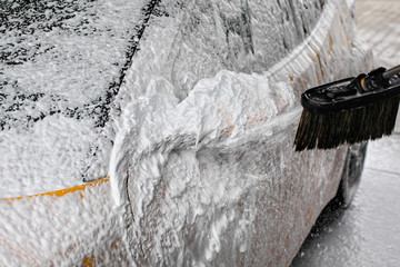 Detail on car side mirror completely covered with soap foam, more spraying from brush, when washed...