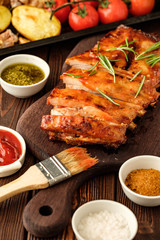 Delicious barbecued ribs seasoned with a spicy basting sauce and served with chopped fresh vegetables on an old rustic wooden chopping board