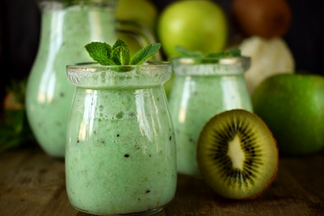 Green smoothie made of kiwi, apple and mint in glass jars surrounded by fruits