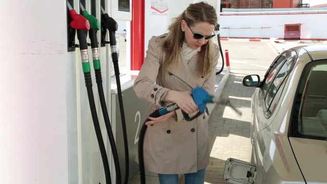 Young woman at a gas station, pours gasoline into a car.