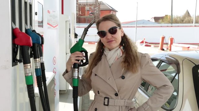 A woman at a gas station brings a gasoline pistol to her head. Expensive fuels, gasoline.