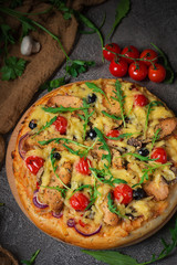 Pizza with chicken, arugula, cheese and onions on wooden rustic table. Top view