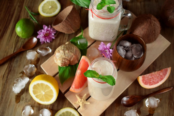 Coconut cocktail in glass jars surrounded by lime, lemon and ice cubes. Top view