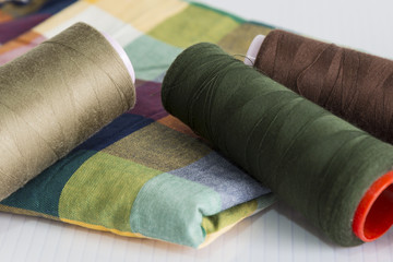 Fototapeta na wymiar brown,green and cream color bobbin on the colorful fabric for textile concept.
