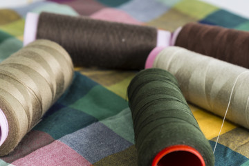 Fototapeta na wymiar brown,green and cream color bobbin on the colorful fabric for textile concept.