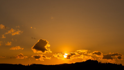 Sun setting behind clouds over forested hills