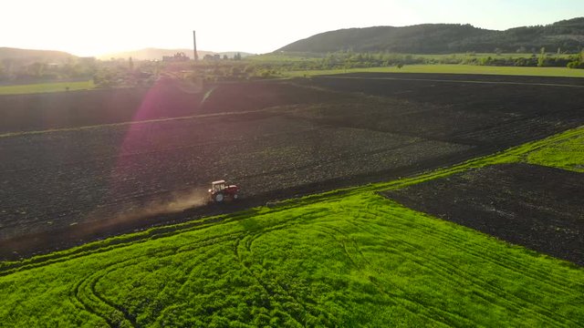 Aerial view of the sunset above the tractor harrowing the field.