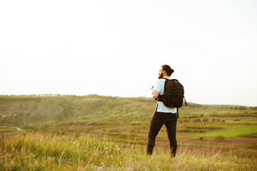 Hipster young man with backpack enjoying sunset on peak mountain. Tourist traveler on background valley landscape view mock-up.Retro filter effect, selective focus.