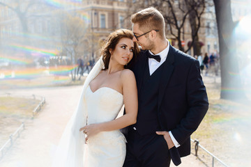 Fototapeta premium Newlywed couple bride and groom photoshoot after wedding ceremony in Saint-Petersburg Russia. White wedding dress with long veil and classical black suit or smoking with bowtie. Businessman in glasses