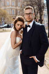 Newlywed couple bride and groom photoshoot after wedding ceremony in Saint-Petersburg Russia. White wedding dress with long veil and classical black suit or smoking with bowtie. Businessman in glasses