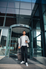 Fototapeta premium Businessman walking from hotel lobby. Full length portrait of young executive with a suitcase.