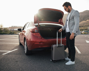 Man traveler putting suitcase in car trunk