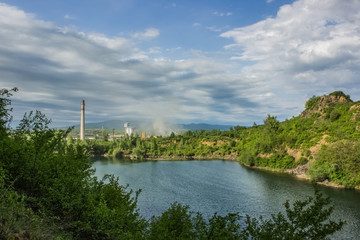 Fototapeta premium soft focus pollution concept with nature quarry landscape and lake on foreground and industrial factory on background