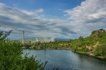 Naklejka na ściany i meble soft focus pollution concept with nature quarry landscape and lake on foreground and industrial factory on background