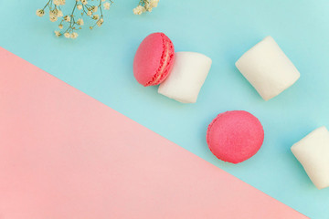 Top view of mini pink macaron or macaroon french desserts cake with marshmallows on soft sweet pink and blue pastel geometric paper flat lay background