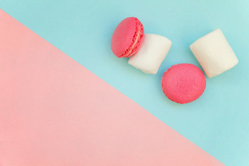Top view of mini pink macaron or macaroon french desserts cake with marshmallows on soft sweet pink and blue pastel geometric paper flat lay background