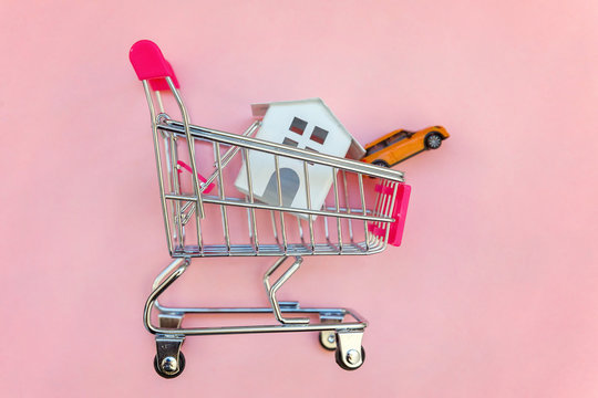 Small supermarket grocery push cart for shopping toy miniature white house and car on pink pastel color paper flat lay background. Mortgage property insurance buy dream home shopping sale rent concept