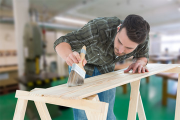 Worker using brush on wooden plank against workshop