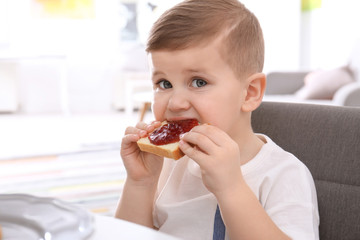 Cute little boy eating toast with sweet jam at table