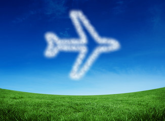 Cloud in shape of airplane against green field under blue sky
